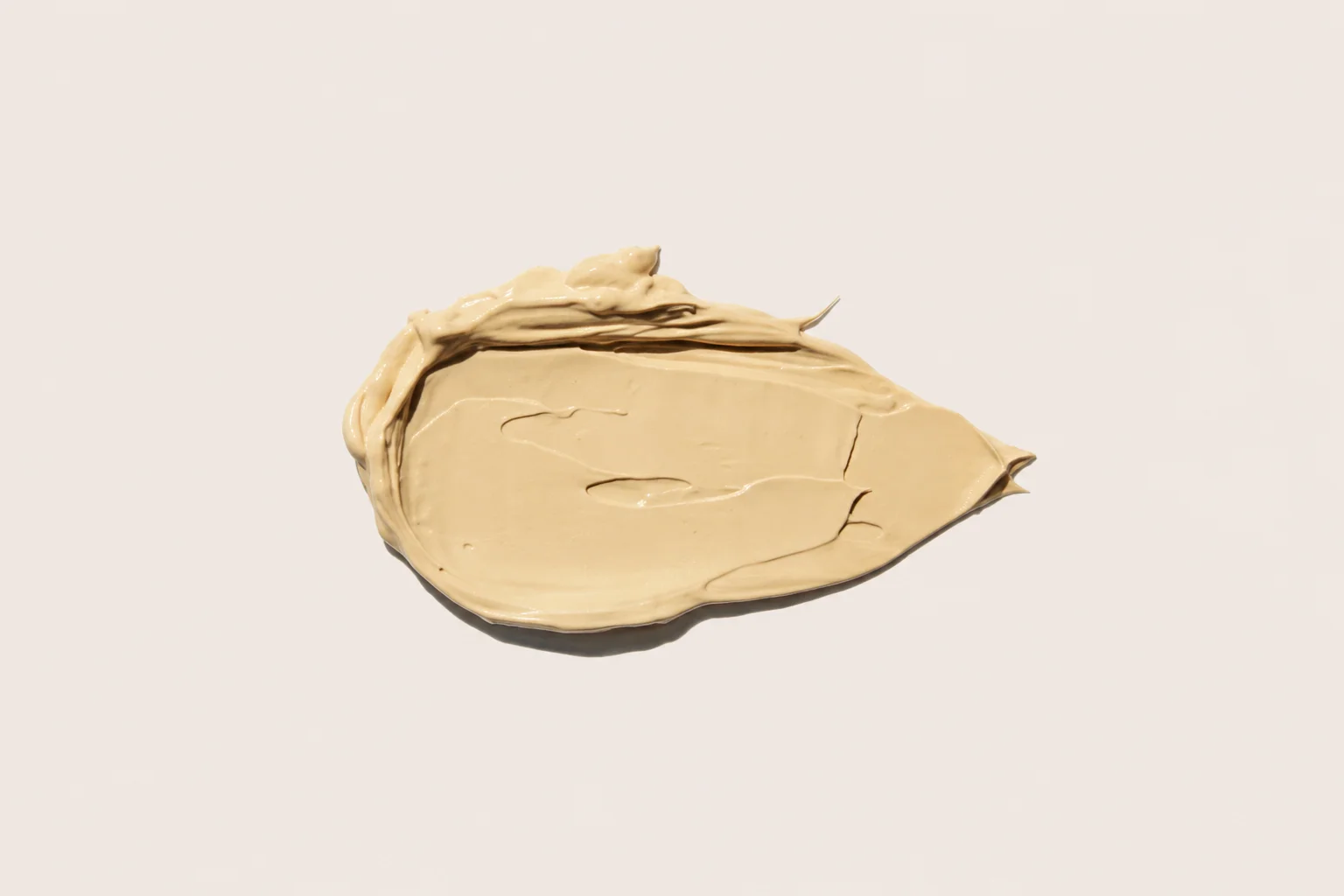A swatch of beige-colored cream or cosmetic product on a neutral light background, showcasing its smooth texture.