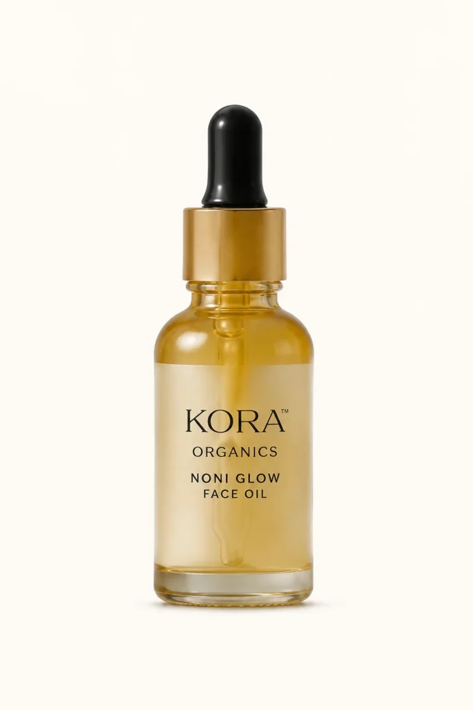 KORA Organics Noni Glow Face Oil in a transparent amber glass bottle with a gold collar and black dropper cap, set against a neutral background.