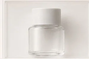 A clear glass bottle with a white cap placed against a plain white background, showcasing minimalist design.