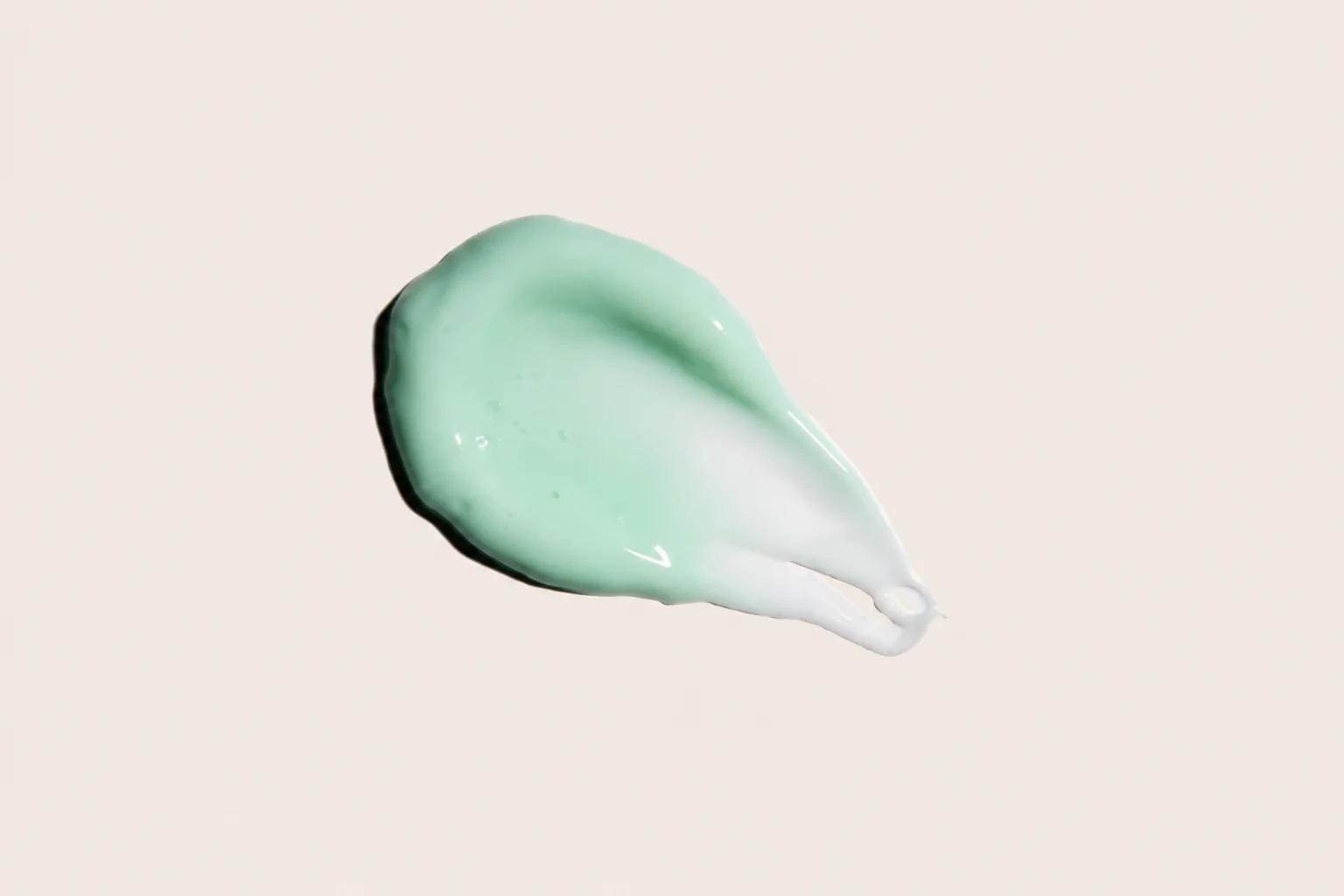 A smooth swatch of mint green and white cream on a light beige background, showcasing its glossy texture.
