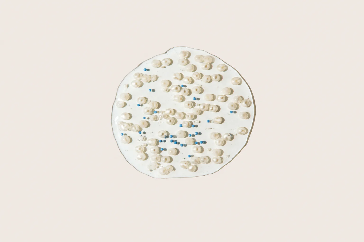 Close-up image of a white cream or gel texture with small pearl-like and blue beads spread on a light background.