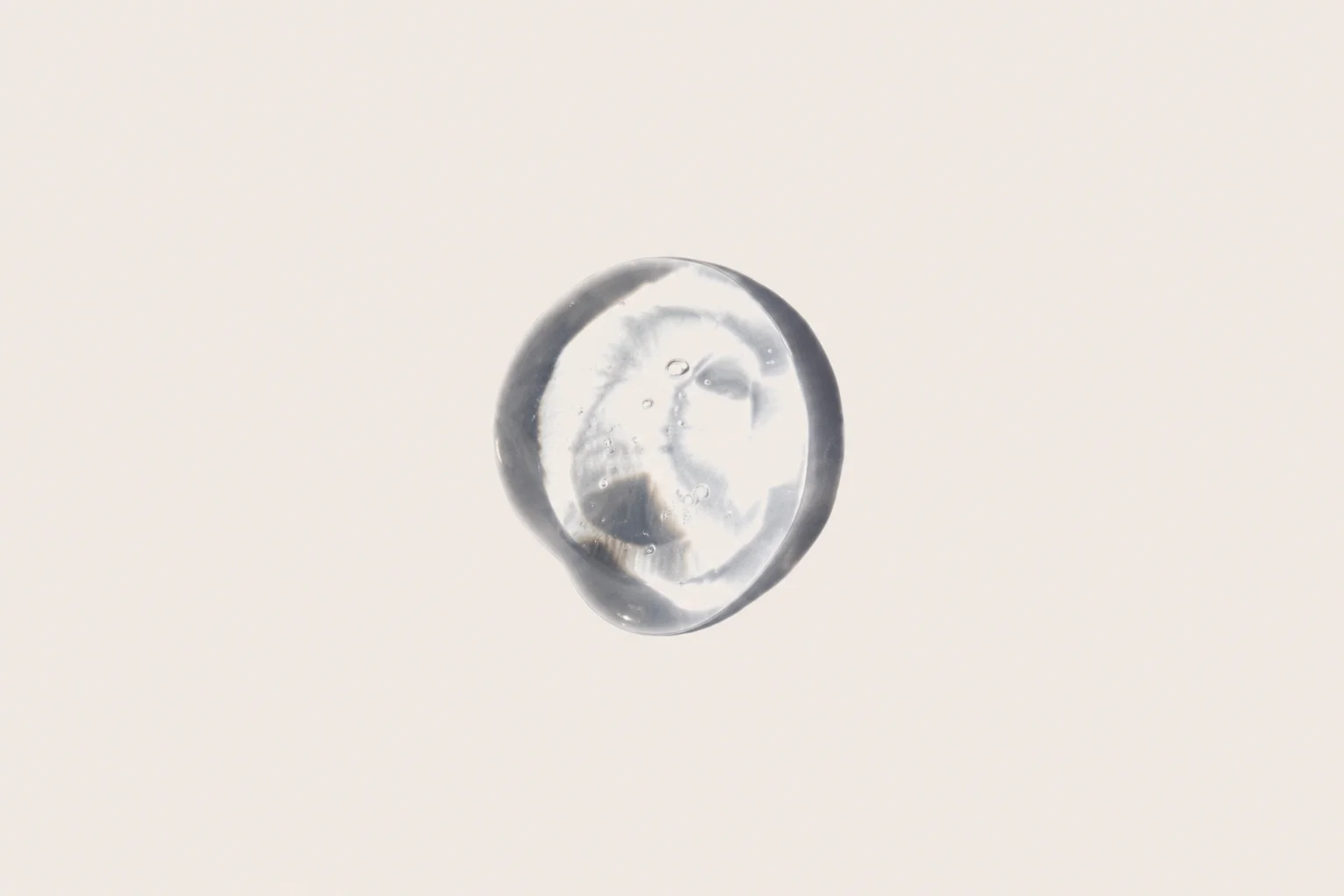 Close-up of a clear, gel-like droplet with a smooth, shiny appearance and a few air bubbles, set against a light background.